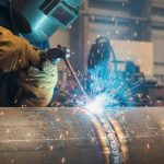 Seorang welder sedang melakukan pengelasan MIG pada pelat logam menggunakan alat las profesional