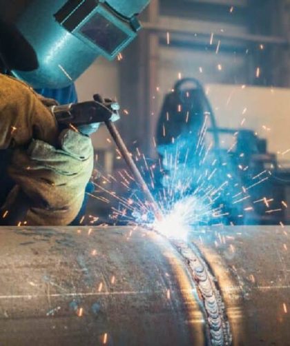 Seorang welder sedang melakukan pengelasan MIG pada pelat logam menggunakan alat las profesional