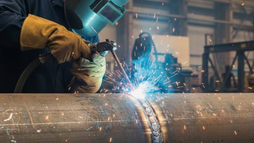 Seorang welder sedang melakukan pengelasan MIG pada pelat logam menggunakan alat las profesional